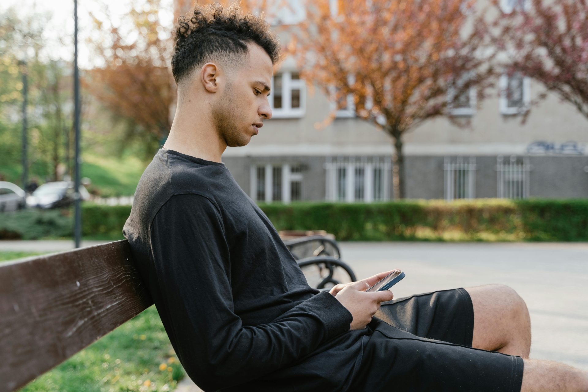 A young adult sitting on a park bench using their smartphone, enjoying a sunny day.