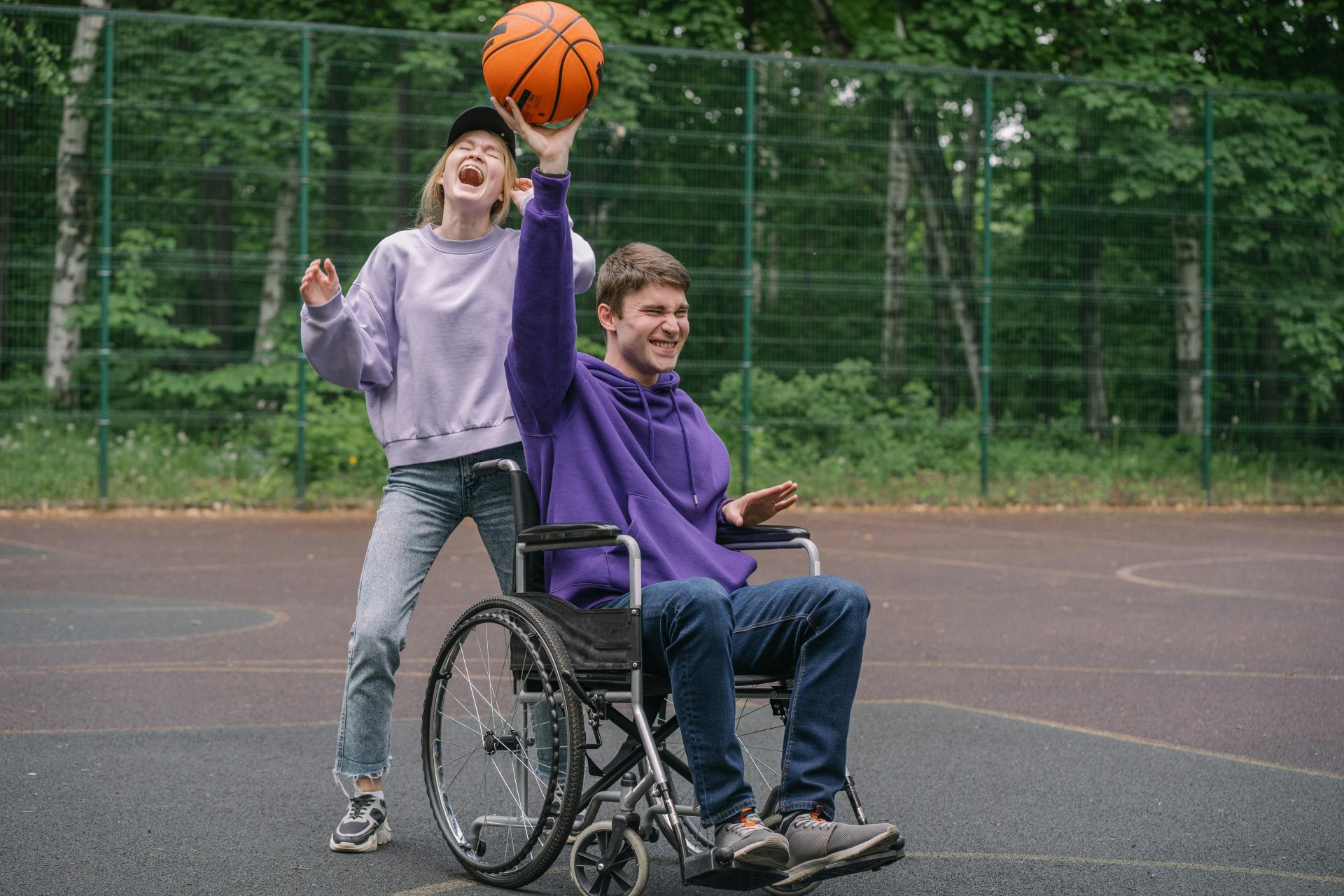A joyful moment of friends playing basketball on an outdoor court, showcasing inclusivity and teamwork.